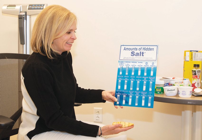 Photo by Nicole Harnishfeger.Suzanne Davis holding a chart showing the hidden salt found in common foods and sauces in her Nutrition and Wellness office at Nantucket Cottage Hospital.