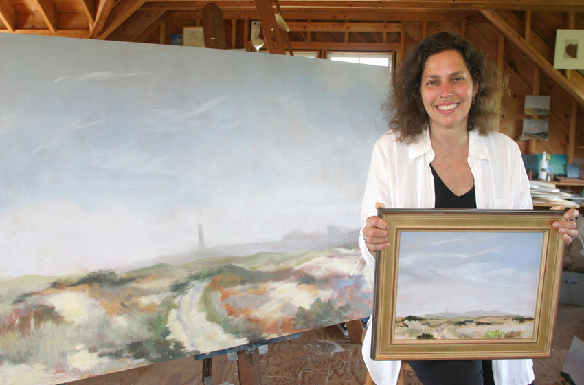 M.J. Dickson holding one version of Great Point at 11 inches by 14 inches and sitting next to a four foot by six foot created by the print in her lap in her studio.