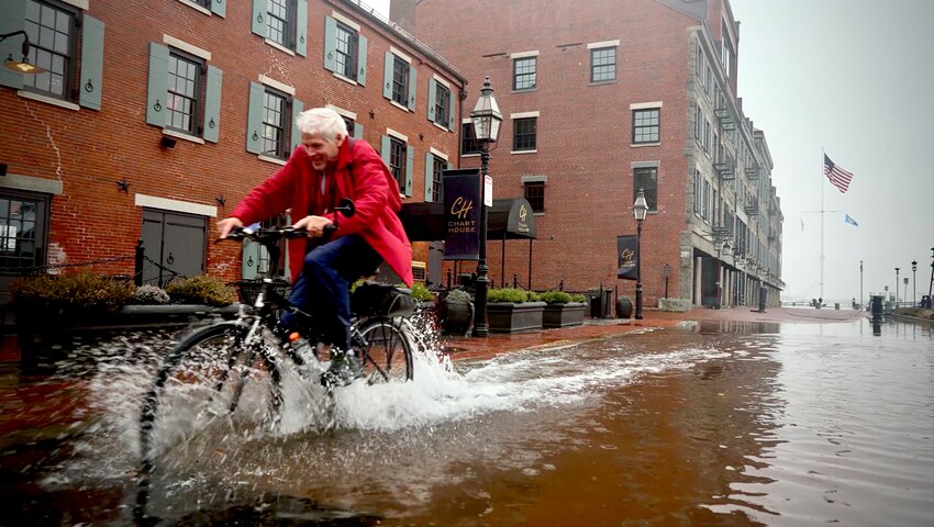 A cyclist pedals down a flooded street near the Chart House restaurant in South Boston.