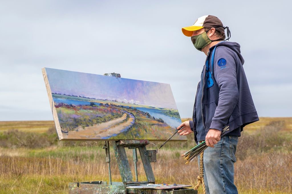 Artist Illya Kagan, wearing a face mask, paints a landscape of Clarks Cove Tuesday morning.