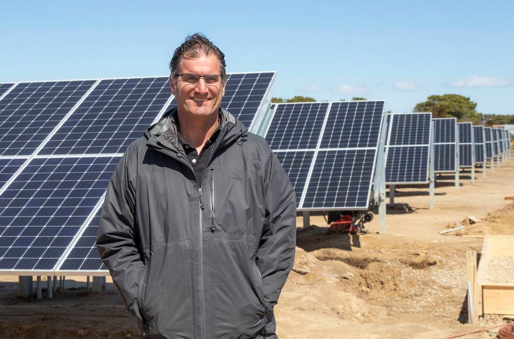 John Bartlett stands in front of some of the new solar panels his farm has installed, dedicating over five acres of open space to renewable energy.