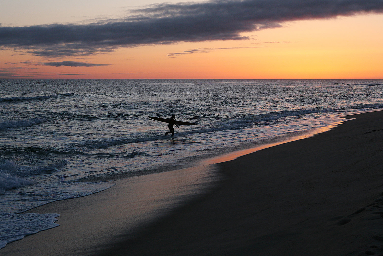 As the sun sets, Jeremy Norwood, of Nantucket, carries his surfboard from the ocean at Cisco Beach on Monday.