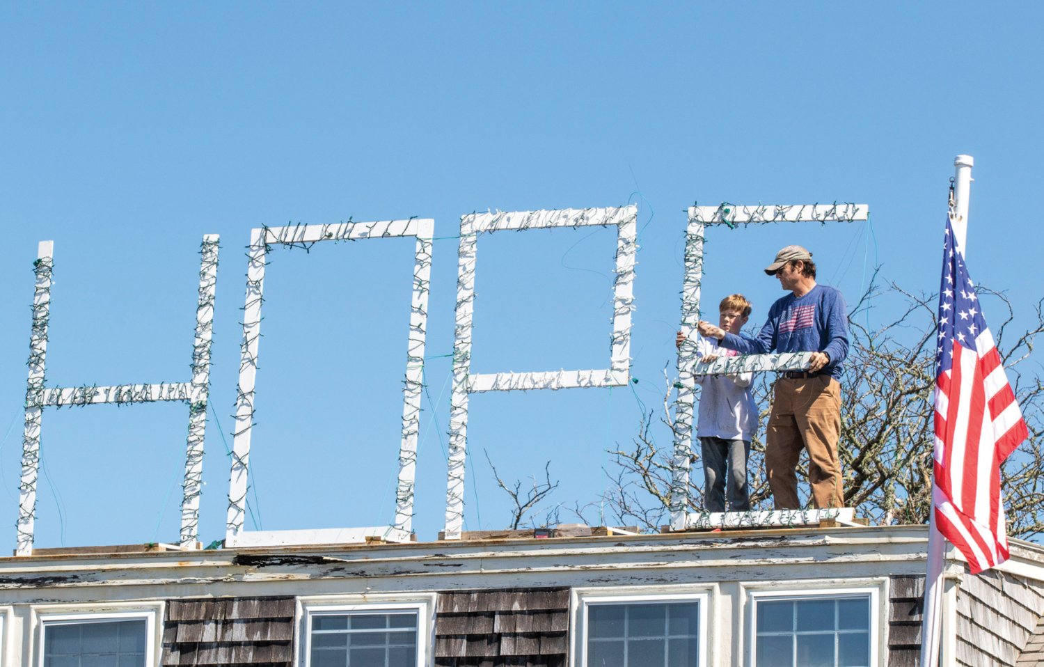 Chris Fraker with help from his grandson Jackson Agnello stands wooden letters spelling “HOPE” wrapped in lights back up on the roof of a Prospect Street home last April following a couple wind storms.