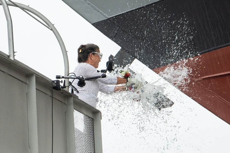 Ship sponsor Polly Spencer breaks a bottle of sparkling wine across the bow during the christening ceremony.