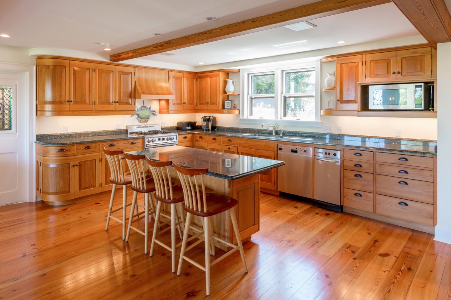 The kitchen has wood floors, an exposed-beam ceiling, a stone-topped center island and counters, and high-end appliances by Viking, Sub-Zero and Miele.