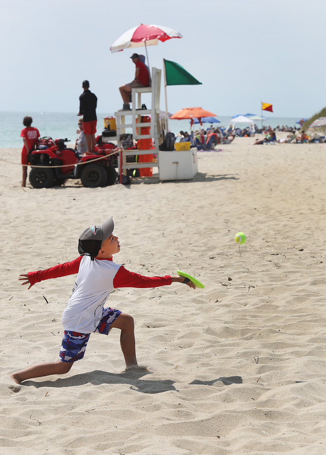 Six-year-old Zachary Luther, visiting with his family from Swansea, plays a game of catch as lifeguards keep watch on a green flag day at Miacomet Beach on the first day of August.