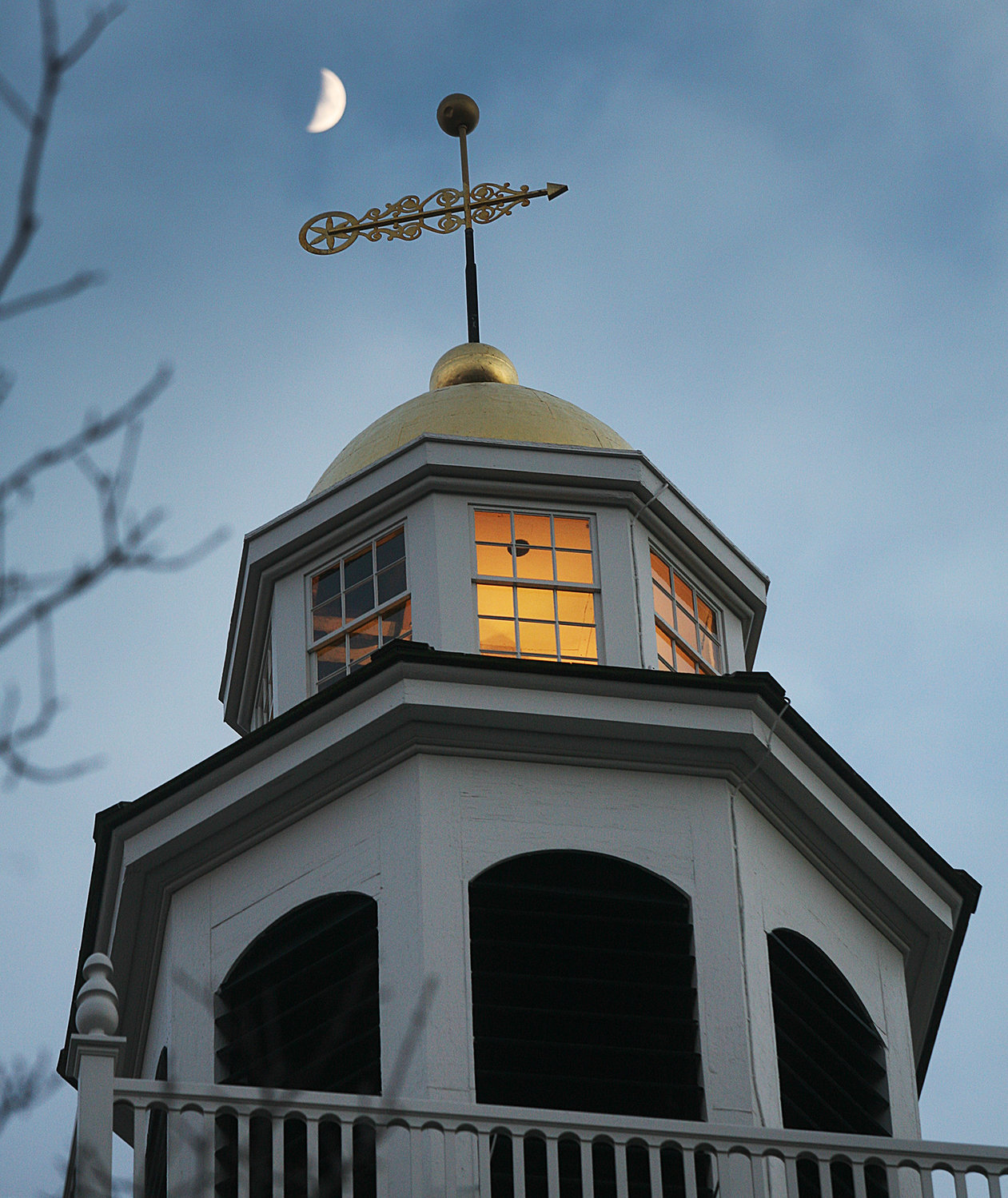The setting sun reflects in the steeple windows of the Unitarian Universalists Meeting House with a waxing crescent moon hovering above in January. Photo by Ray K. Saunders