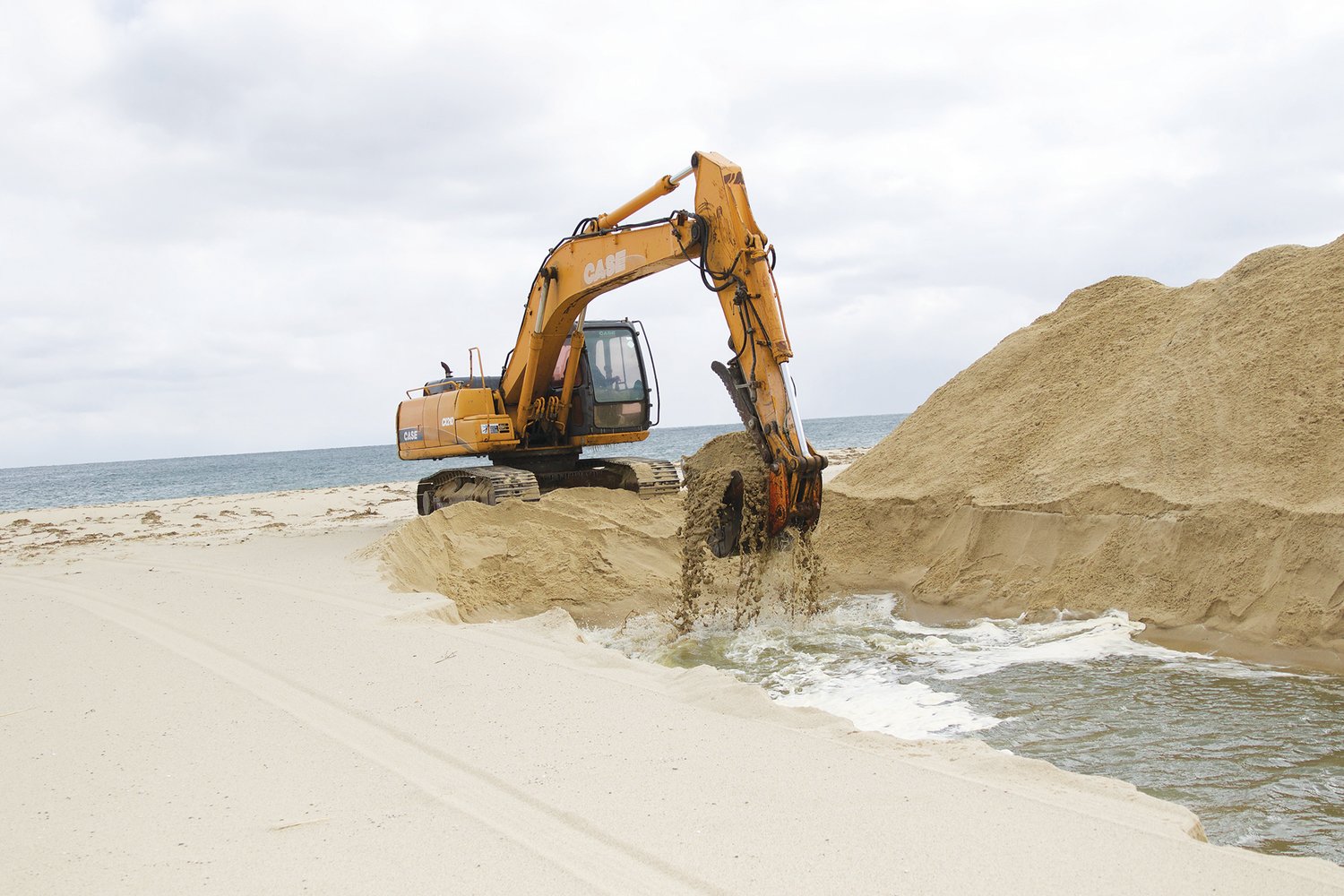 An excavator digs a path from Sesachacha Pond to the ocean Monday.