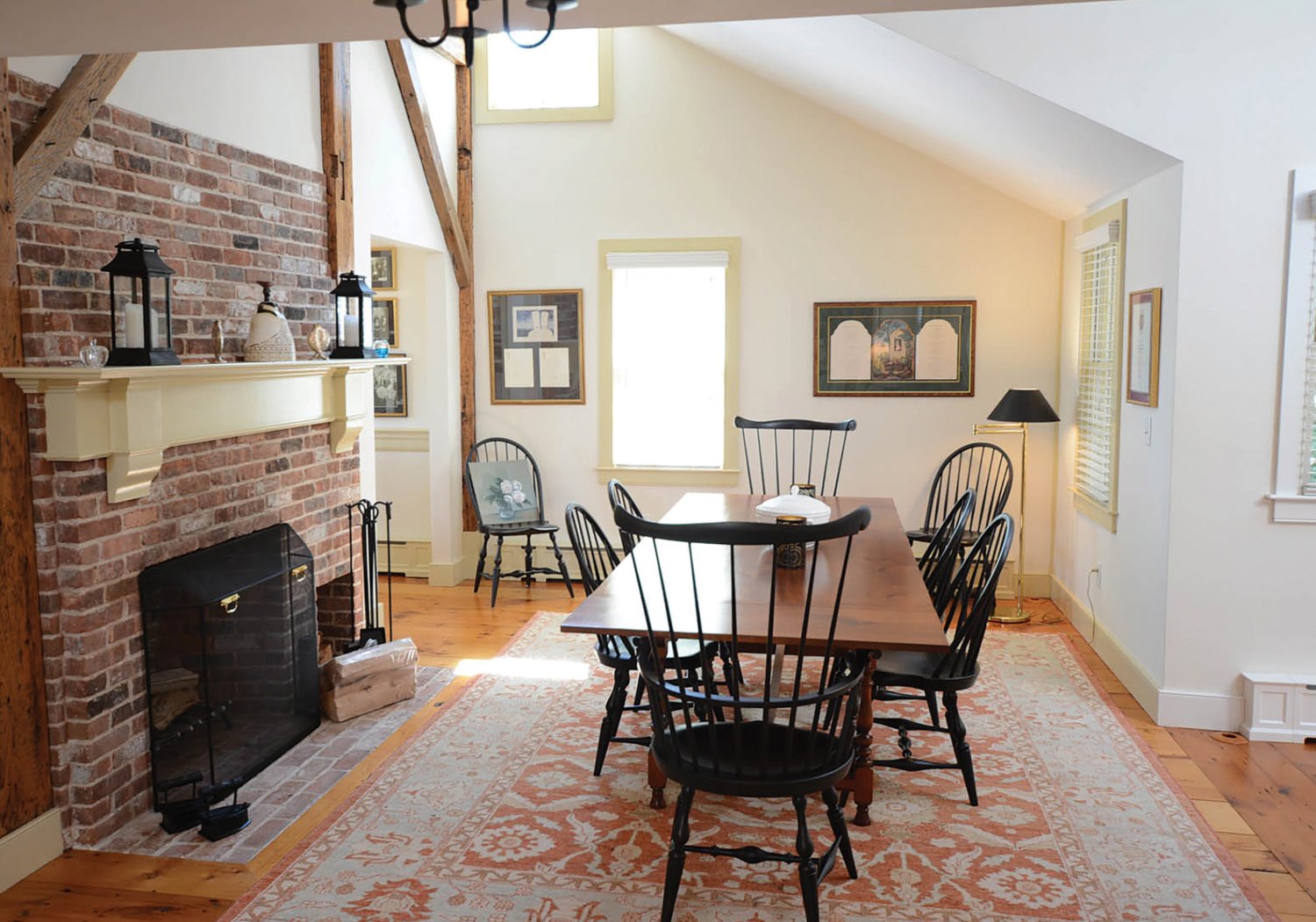 The dining room has a vaulted ceiling, wide pine floors, a brick fireplace with a brick hearth and exposed beams.