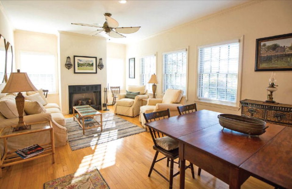 The living room in the cottage has wood floors, multiple windows and a fireplace.