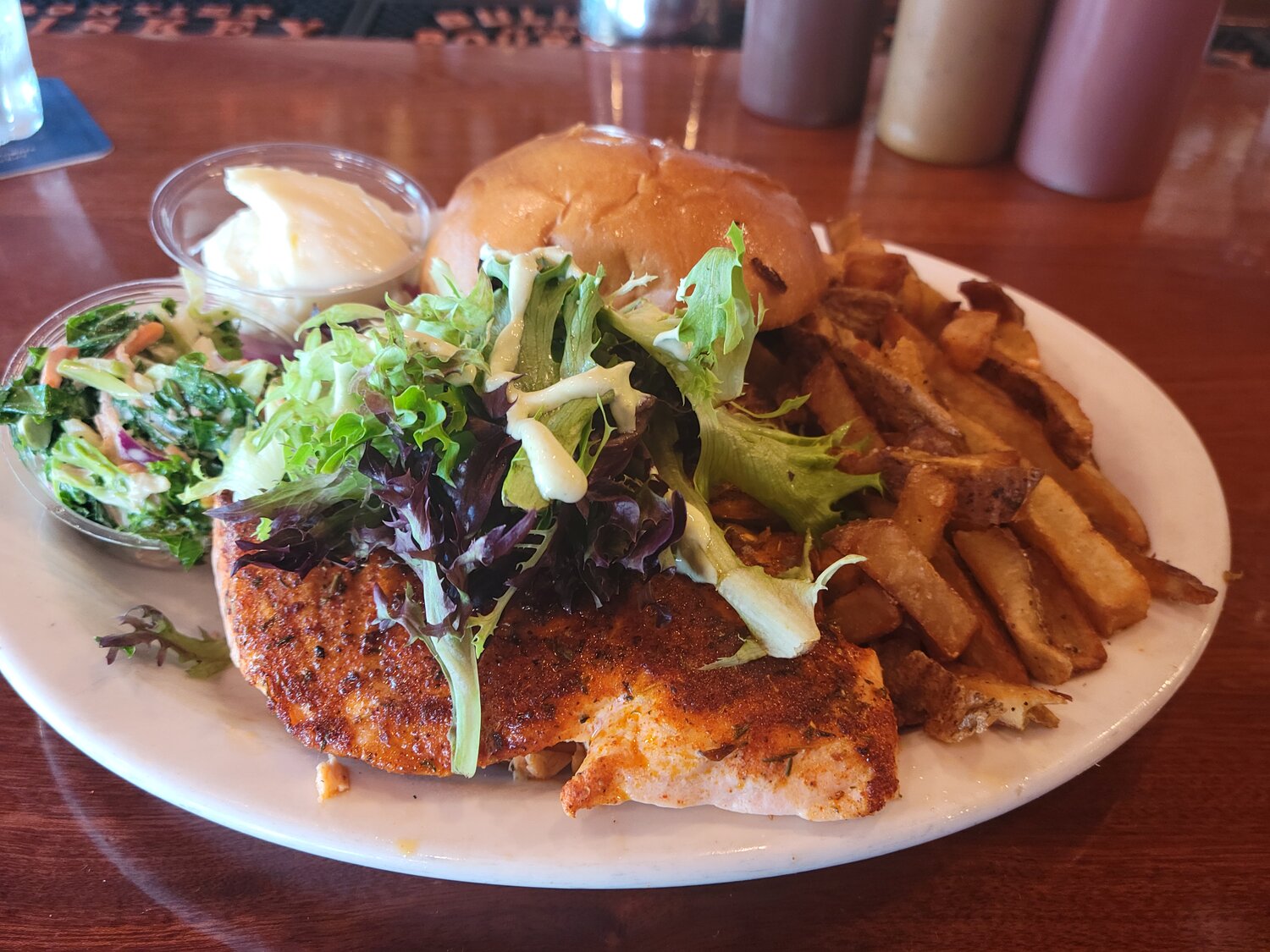 The blackened salmon sandwich is served with a side of coleslaw and topped with fresh greens and a cilantro crema.