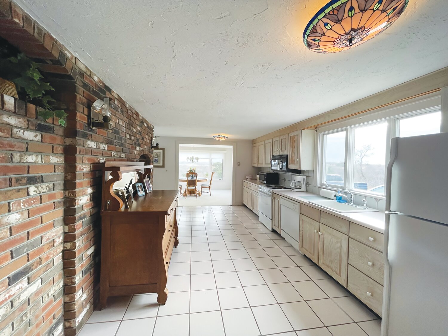 The kitchen and living room are divided by a brick fireplace. The kitchen has tiled floors and plenty of counter and cabinet space.