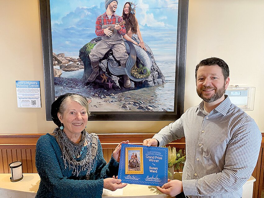Susan Ward stands below the painting believed to be of Ivar Haglund’s parents. General manager Greg Covey presents Ward with her prize of a year of fish ‘n chips and chowder.