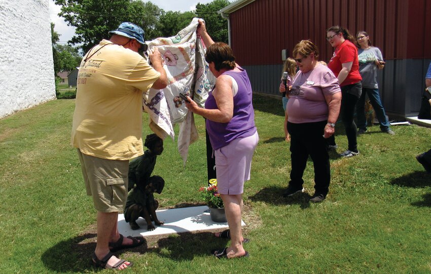 The National Orphan Train Complex unveiled its 52nd orphan train statue on Saturday, June 14, in Jamestown, Kansas, in front of the city offices. The new orphan train statue is of orphan train riders, brothers James and Charles Hill. Carolyn Peterson (middle), granddaughter of James Hill, received a quilt made by another Hill descendant, which hid the statue before the unveiling.