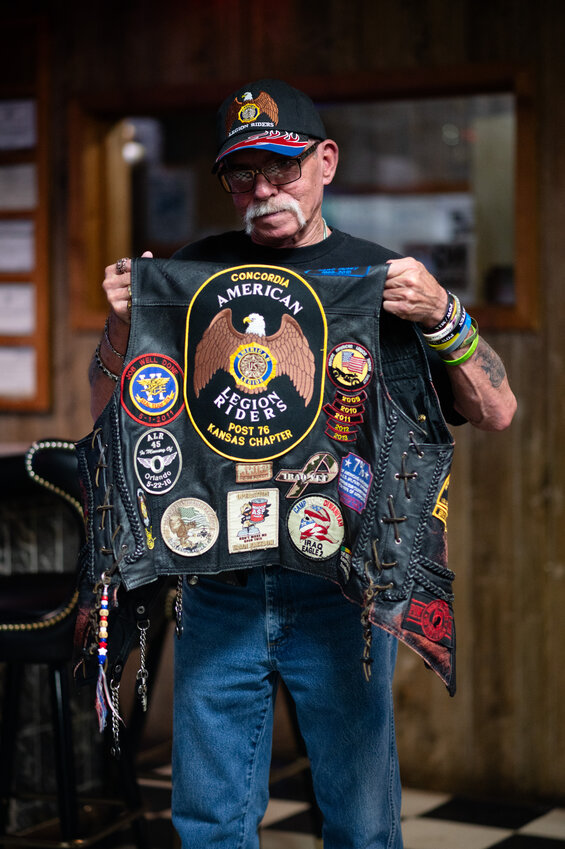 Rick Simpson holds up his decorated vest while standing in the main bar area at the Concordia American Legion Post 76 on Monday, May 19, in Concordia, Kansas.