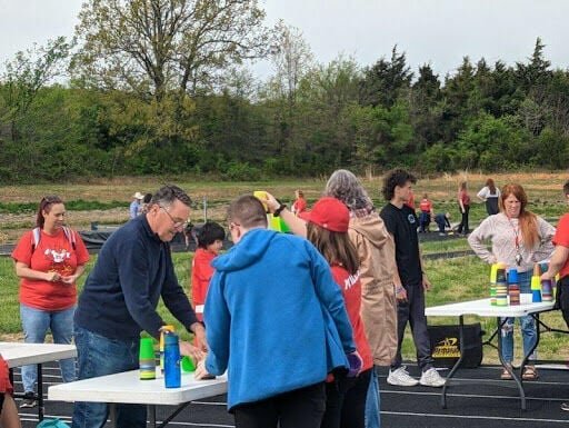 Representative Mike Stephens assists students with a cup stacking activity during the Southwest Conference Field Day that was hosted by Pleasant Hope Schools on Friday, April 21. For more about this story, see page 10.