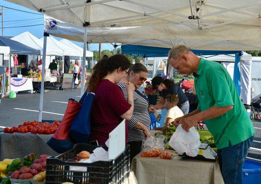 Jim Parker of Parker Farms weighs and bags the produce for two customers at the Greater Polk County Farmers Market on Saturday, July 22.