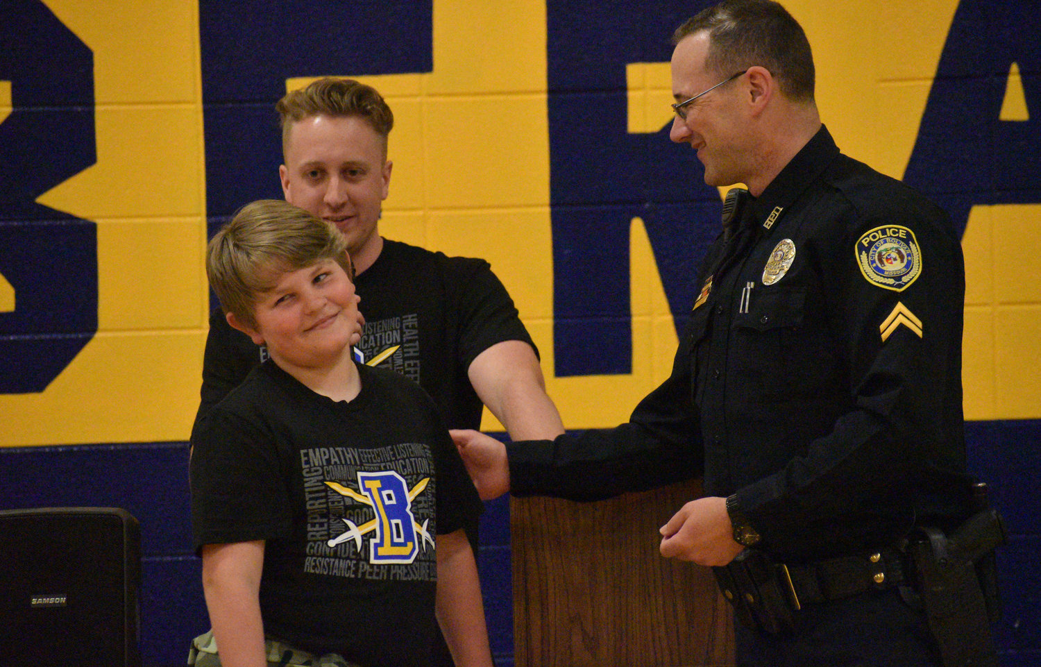 Fifth-grade teacher Jacob Allee and Cpl. Scott Hendrickson look on as D.A.R.E. graduate Jeffrey Stormant flashes a smile at his friends.