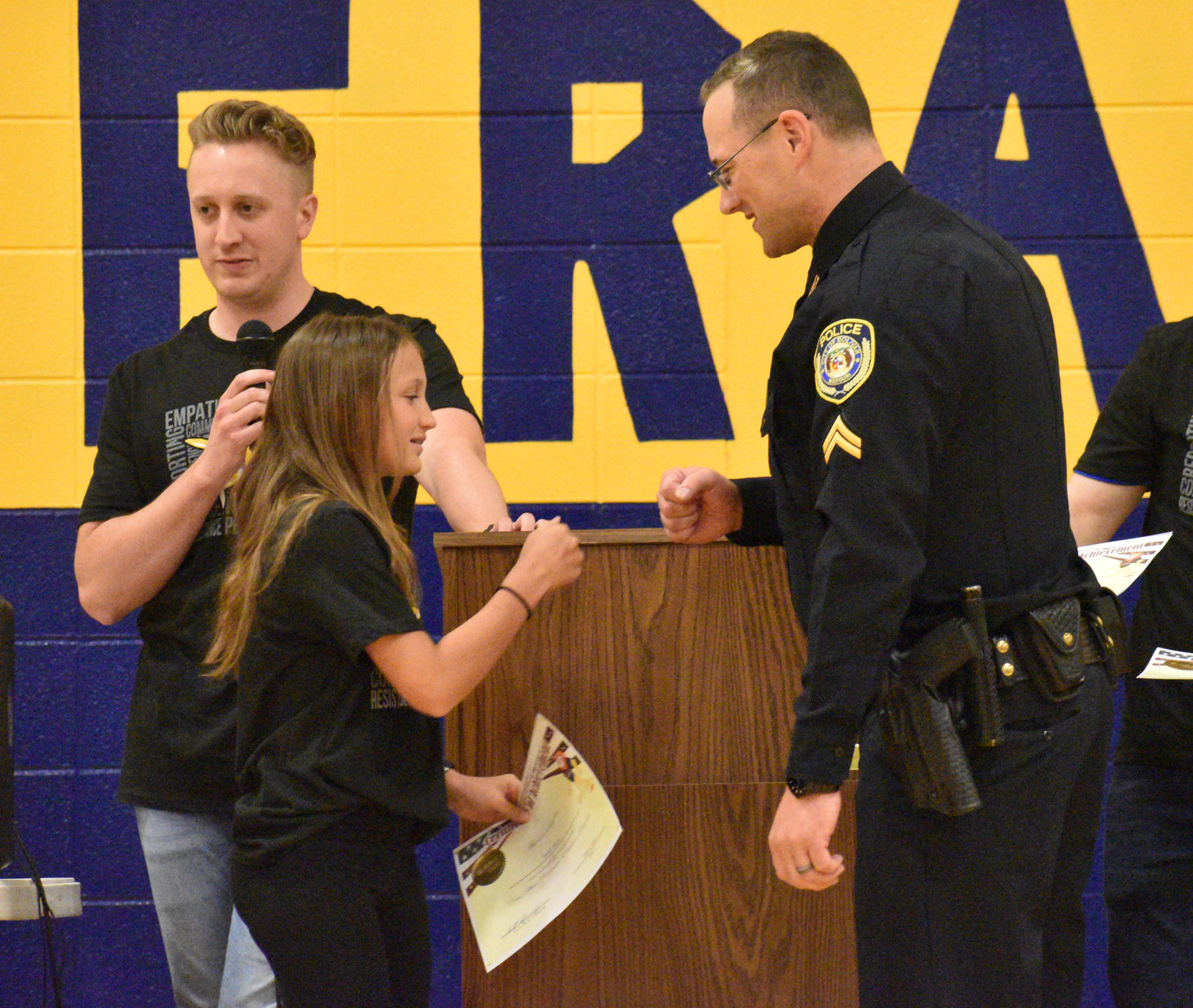 Taylor Mann gives Cpl. Scott Hendrickson a fist bump after he hands her a diploma. Also pictured is teacher Jacob Allee.