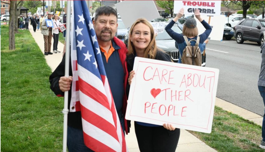 Tom Osina, a Manassas City councilmember, and Jill Spall, a Manassas School Board member, pose for a photo while holding an American flag and a sign.
