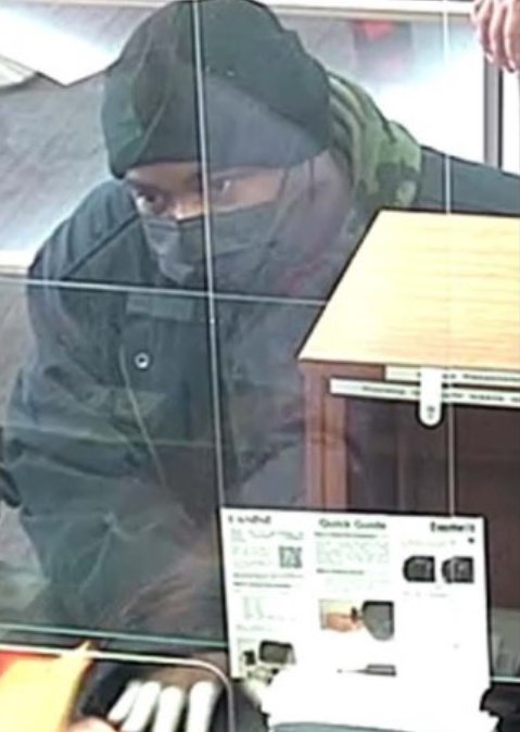 The robber stands on the other side of the teller's glass shield while demanding money.