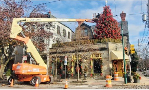 Eric Graber and his crew use an orange boom lift to string the lights and position the red bows, with holiday music  playing during the decorating.