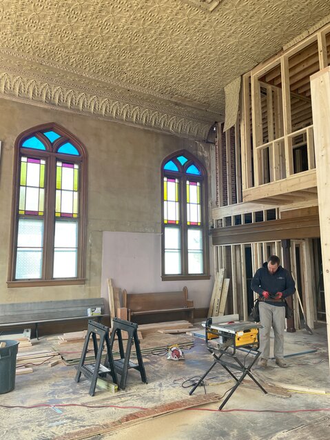 Workers renovate an impressive great room with beautiful stained-glass windows and high tin ceilings.