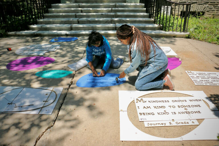 Anshika Lal (left) and Caprice Jackson, of nonprofit workshop Tiny WPA, install the Rain Poetry exhibit at Vernon Park. Some of the haiku, written by elementary students, will be permanently visible. Others will be revealed only when they get wet.