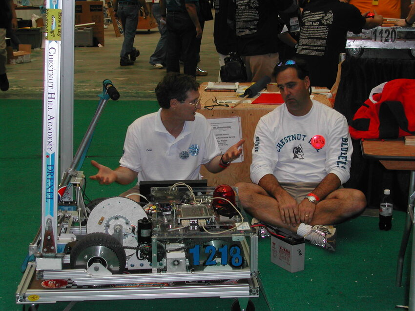 Peter Randall and Rob Ervin, co-founders of Springside Chestnut Hill Academy's Robotics and Engineering Department, sit on the floor of the Astrodome in Houston, Texas, at SCH's very first robotics World Championship.