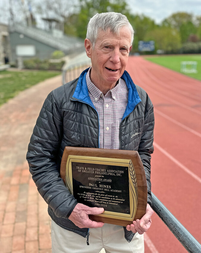 Retiring Springside Chestnut Hill Academy coach Paul Hines is pictured on the track bearing his name with the Association Award presented to him recently by the Track &amp; Field Coaches Association of Greater Philadelphia.