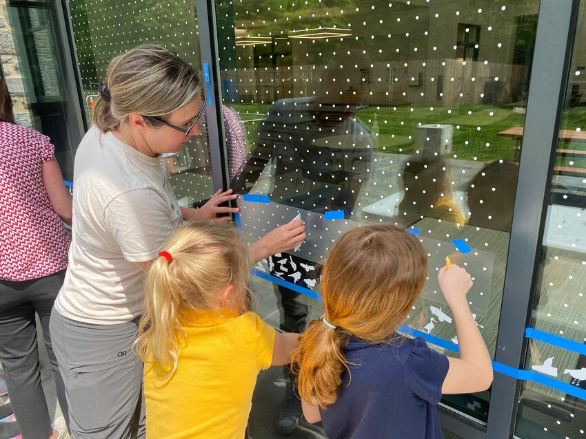 Bird biologist and SCH parent Stephanie Egger helps third graders install thousands of Feather Friendly dots on the windows of the Lower School cafeteria.