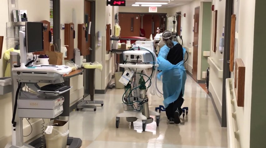 A HEALTH CARE WORKER WEARING A PROTECTIVE GOWN moves respiratory equipment toward a patient room on a COVID unit inside Mercy Hospital in Springfield.