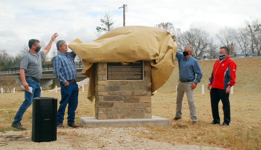 MARKER UNVEILED &mdash; From left, Spencer Jones of Great River Engineering and Scott Bilyeu, John Elkins and Ed Addington of the Ozark Special Road District pull back the canvas to unveil a marker that celebrates the history of the Riverside Bridge.&nbsp;