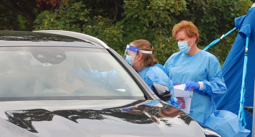 A HEALTH WORKER FROM COX HEALTH administers a COVID-19 test to a patient in her car with assistance from the Christian County CERT volunteer at a drive-through test site in Ozark on Sept. 10, 2020.