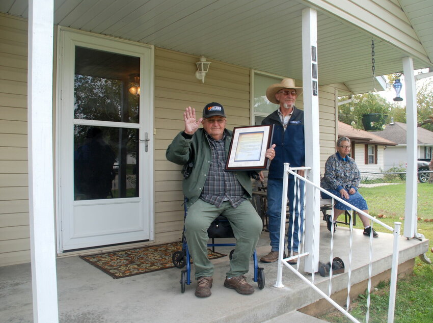 Herschel Walles waving from his front porch with his Wave to Your Neighbor Day proclamation.