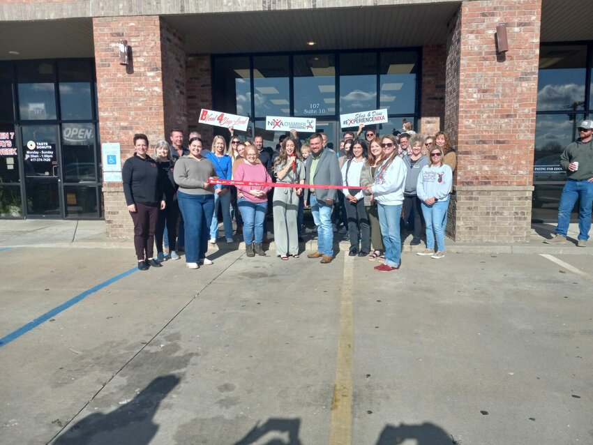 Friends, family, and supporters from the Nixa Area Chamber of Commerce gather with Katrina Hagan (with scissors) as she cuts the ribbon at the ceremony celebrating the new location of Sensitively Sweet Bakery.