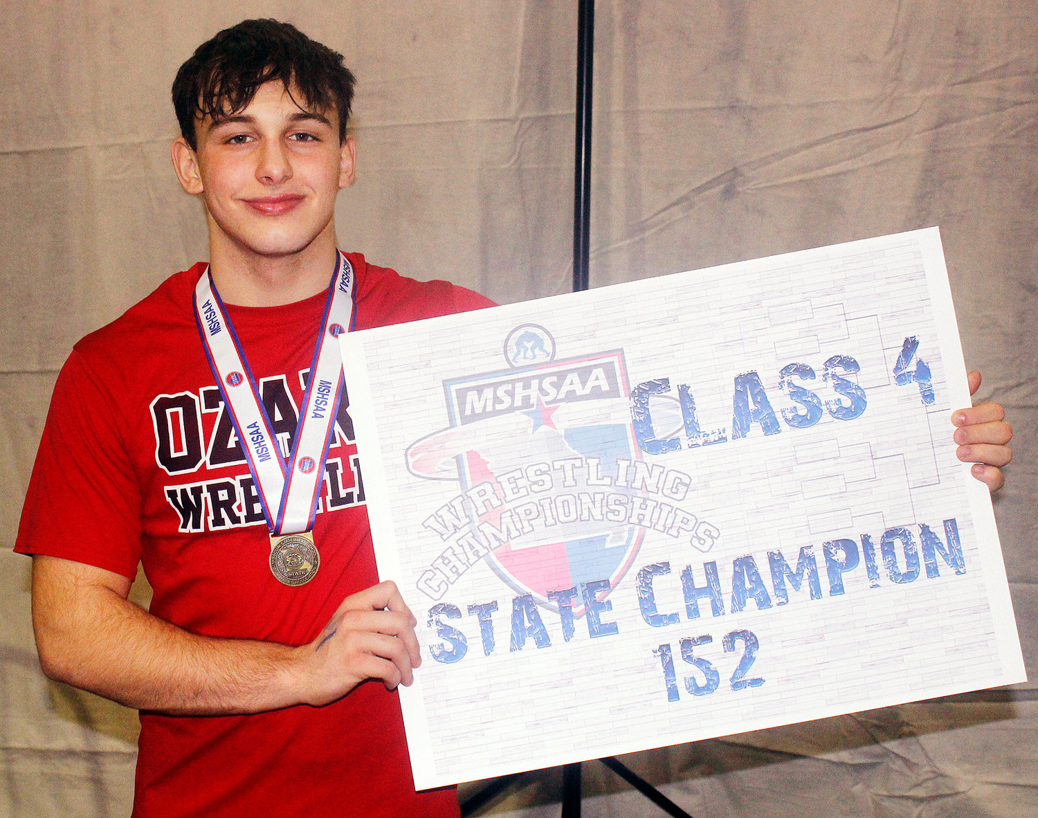 BRAXTON STRICK shows of his medal and state championship placard.