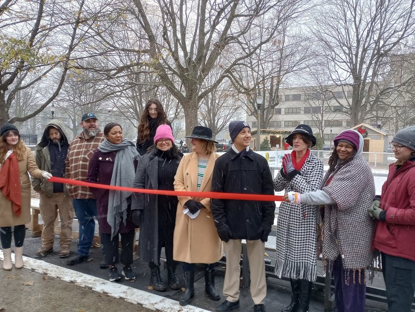 Lansing Mayor Andy Schor and the team from Downtown Lansing, Inc. prepare to cut the ribbon to open the Kringle Holiday Market in Reutter Park. He was also joined by vendors as well as individuals who helped build the vendor buildings.