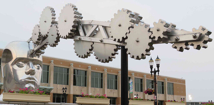 “Portrait of a Dreamer” (aka “The Gearhead”), Iler’s monumental sculpture at the crossing of Michigan Avenue and Museum Drive in downtown Lansing, deftly meshes mid-Michigan’s manufacturing prowess, represented by gears, with its high-tech brainpower, embodied in the figure’s huge cranium. 