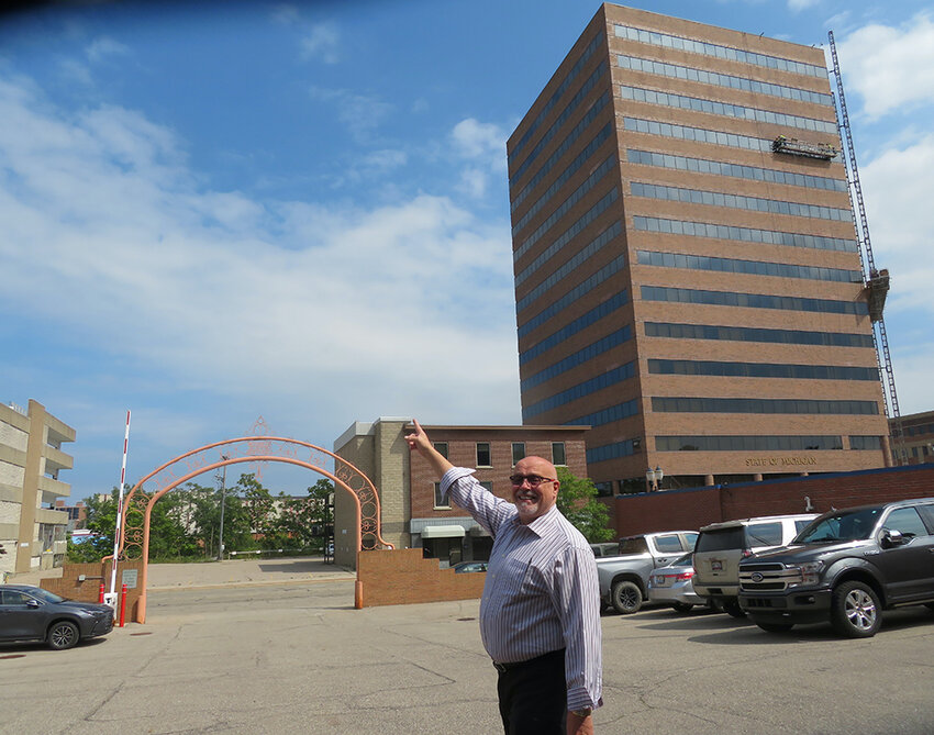 Paul Gentilozzi in the parking lot of the Atrium Building, pointing across Grand Avenue to where he intends to build Tower on Grand, which at 25 stories would become Lansing’s tallest building. 