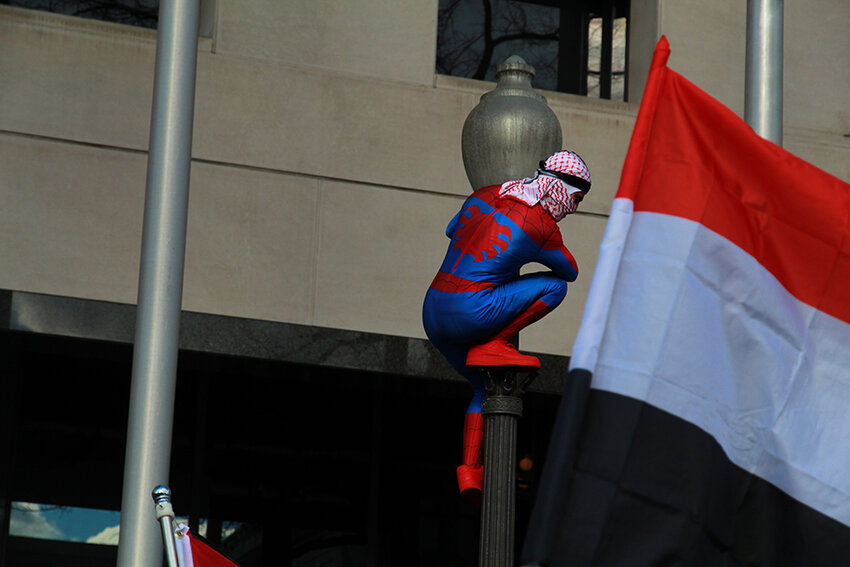 A protester known to those around him as “Palestinian Spiderman” scales a lamp post at Freedom Plaza.