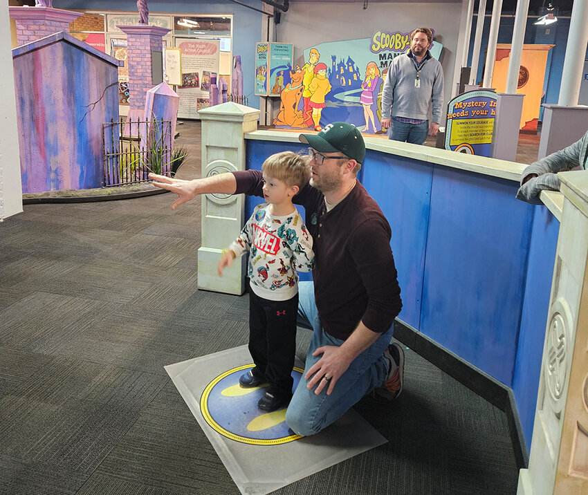 Lansing resident Alex Dethloff guides his son in the “Ghost Chase” portion of the exhibit, while Impression 5 executive director Erik Larson looks on from behind.