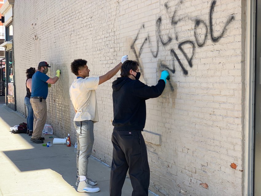 Volunteers scrub graffiti off a wall of a building this morning on Allegan Street between Washington Square and Grand Avenue as part of a clean up organized by Downtown Lansing Inc.