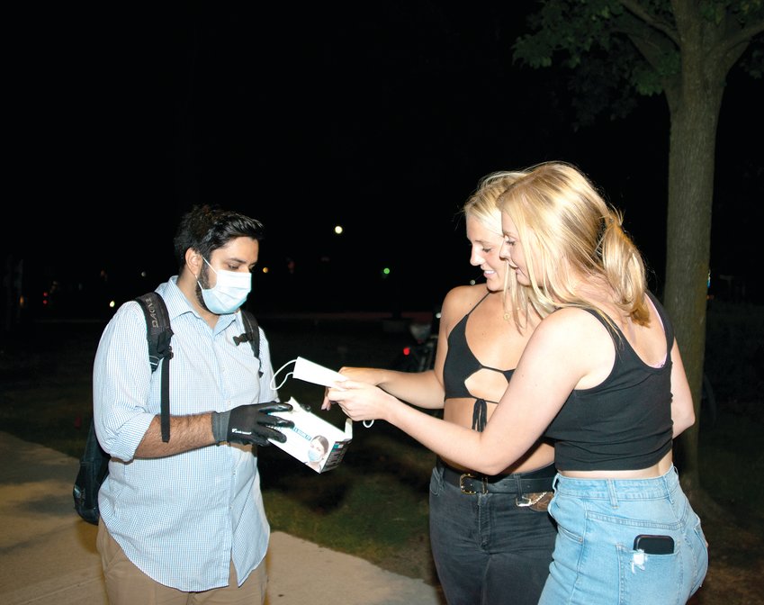 East Lansing Mayor Aaron Stephens hands out disposable face masks to party-goers in downtown East Lansing on Saturday night of Welcome Weekend.