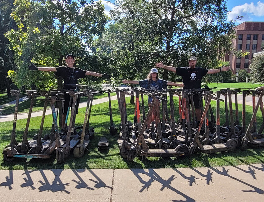 Cal DuLow (right) and his daughter, Alani (center), and son, Xan, pose on the campus of Michigan State University with some of the scooters they found in the Red Cedar River this summer.
