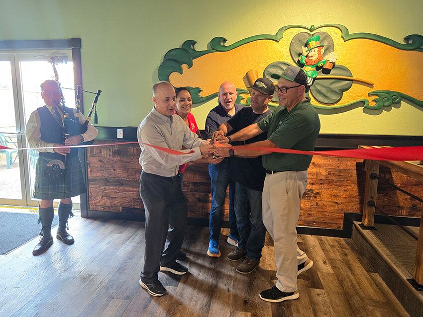 From left: William Collins plays the bagpipes at the Irish Pub’s Tuesday (July 16) grand opening as Lansing Mayor Andy Schor, general manager Stephanie Robinson and co-owners Jeremy Werner, Dave Meredith and Brian Leyrer cut the ribbon.