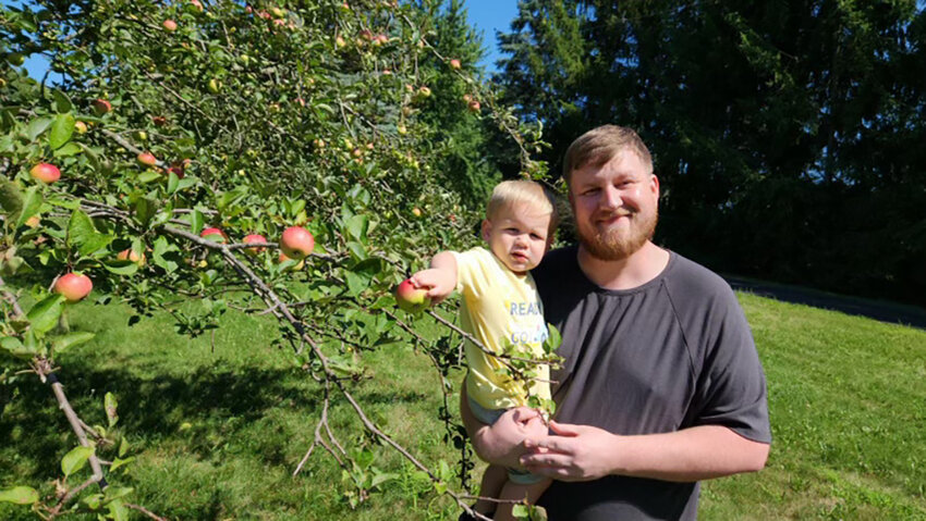 Mason McNair, the new director of MSU&rsquo;s Horticulture Gardens, and his son, Miles, pose in front of an apple tree at their home in DeWitt.