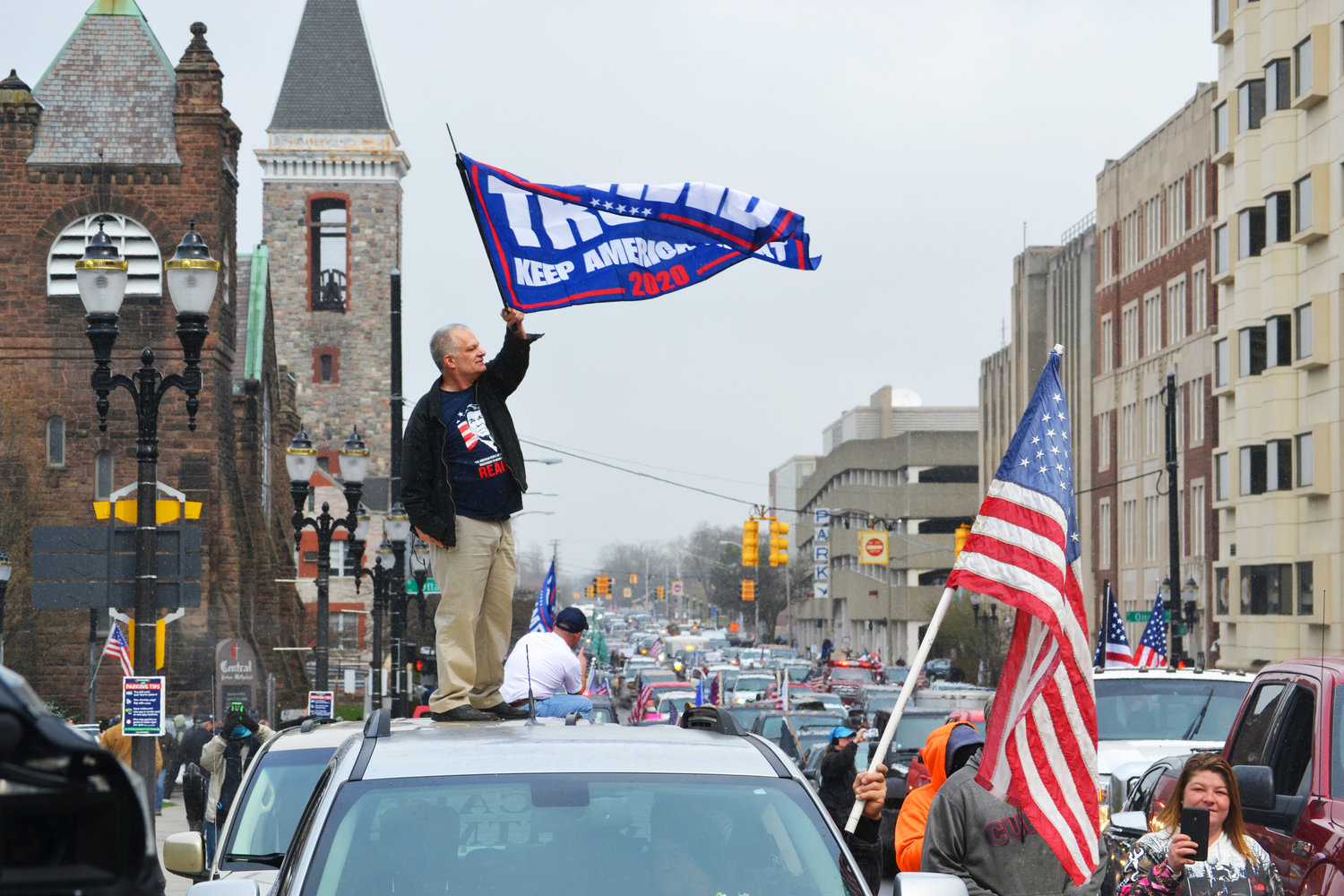 A man waves a Trump flag atop his vehicle.