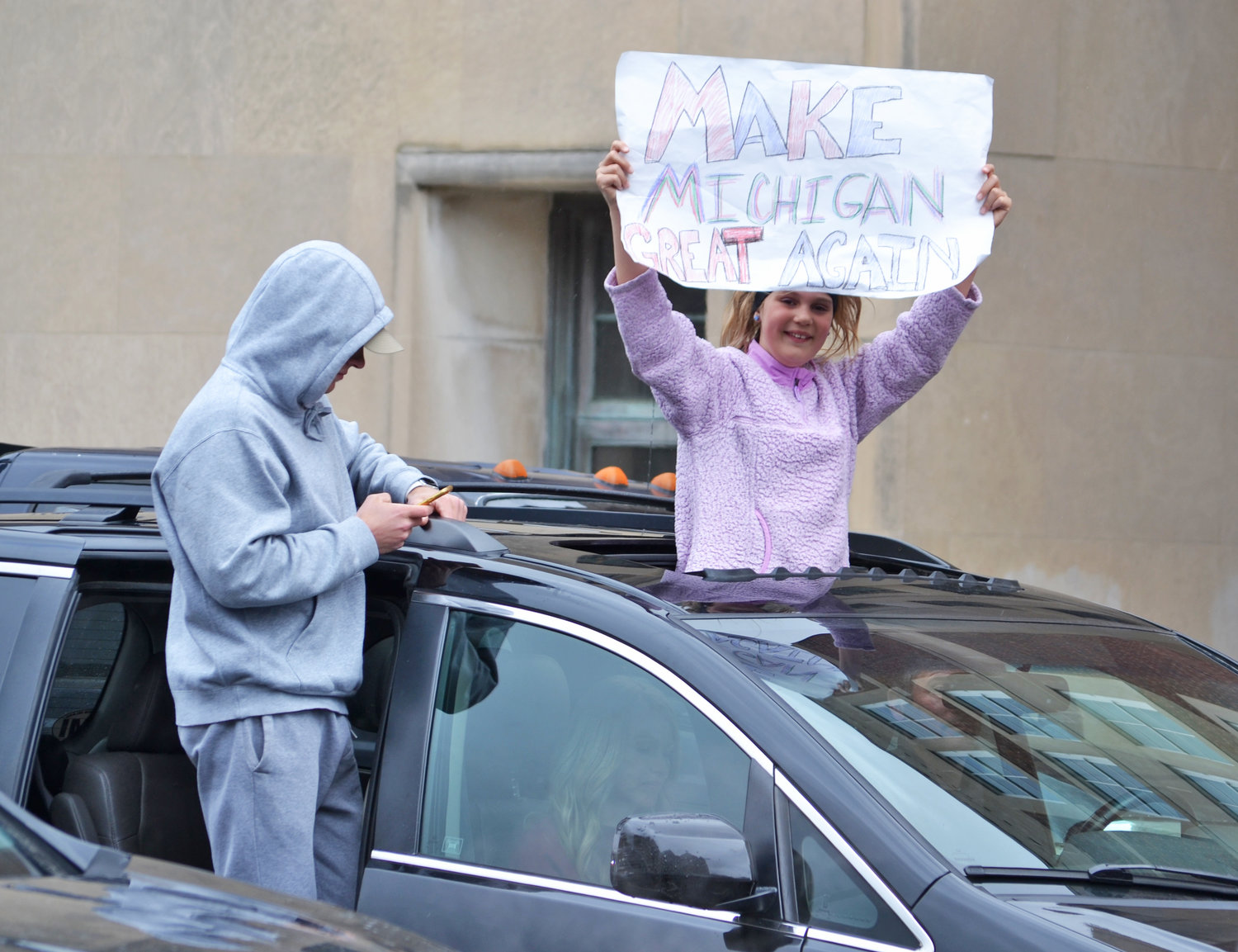 A young woman with a sign reading "Make Michigan Great Again."