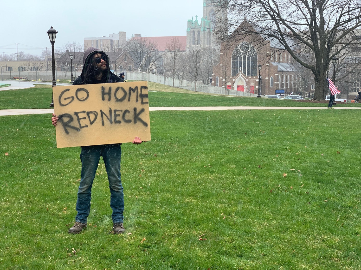 A man with a sign reading "Go Home Redneck."